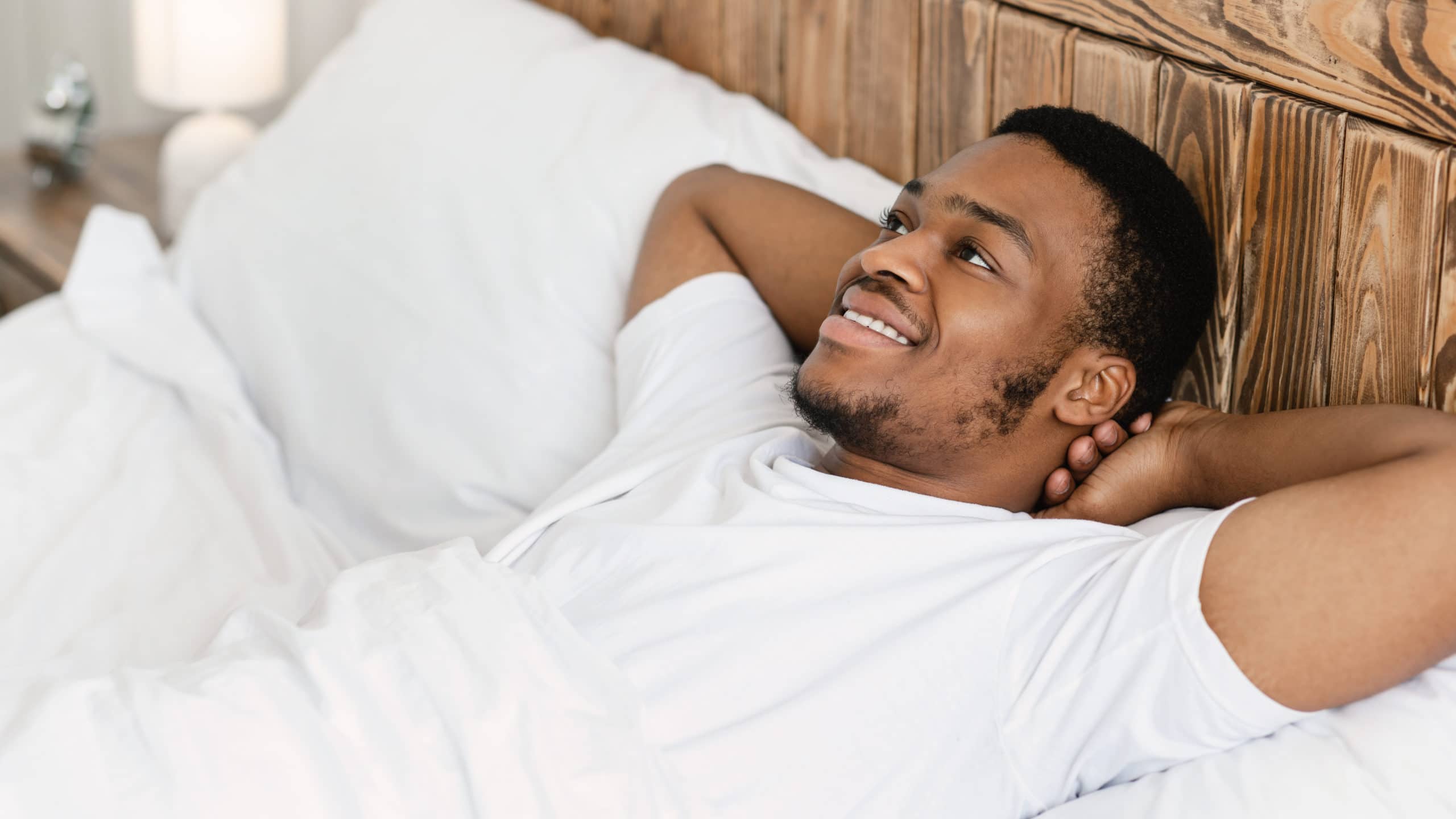 Glücklicher Afrikaner Mann, der am Morgen wach im Bett liegend