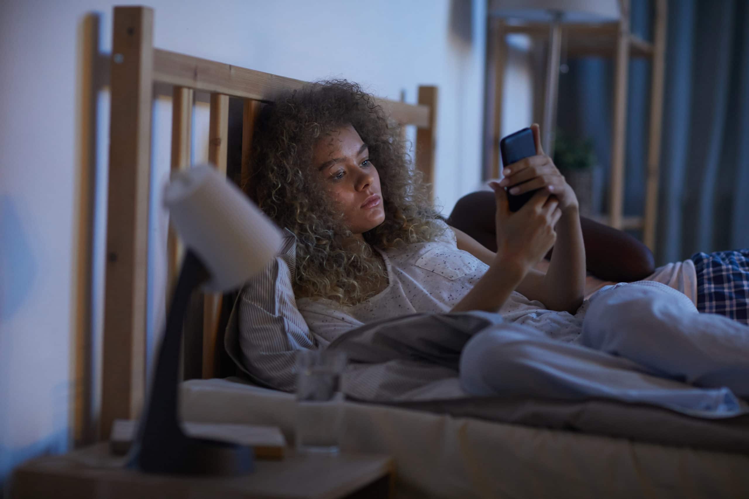 Junge Frau mit Smartphone im Bett