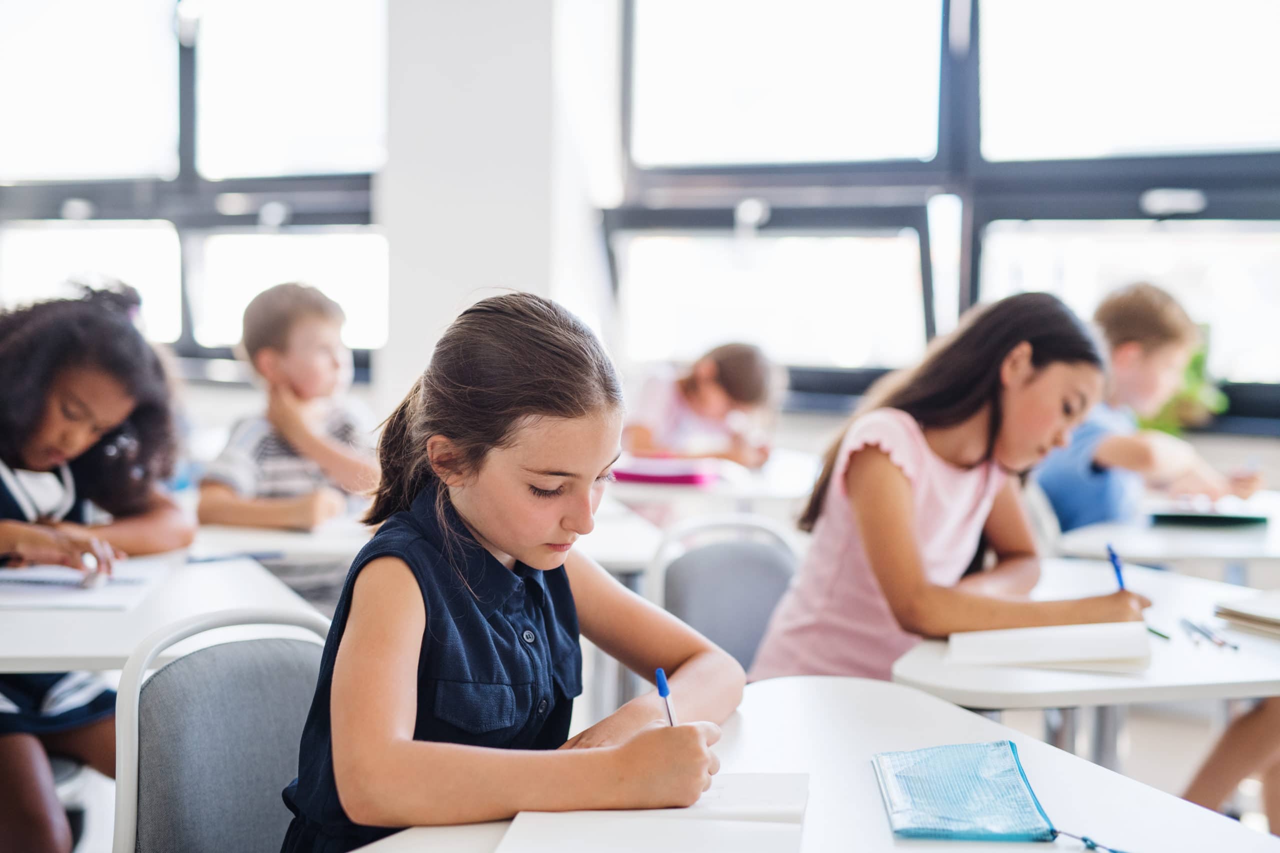 Konzentrierte kleine Schulkinder sitzen am Schreibtisch im Klassenzimmer, schreiben