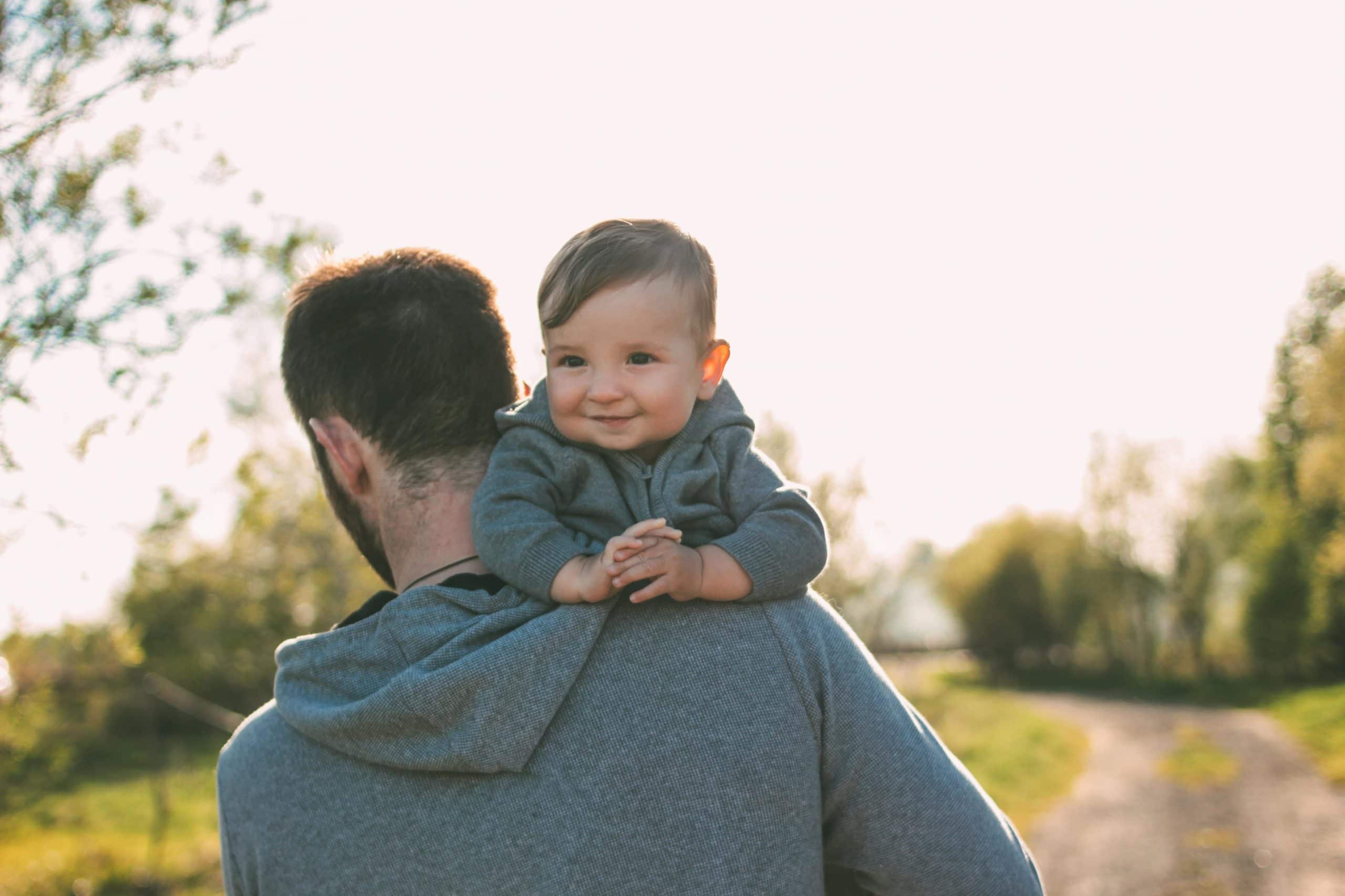 Niedliches Baby 8-9 Monate auf den Schultern seines Vaters im Freien