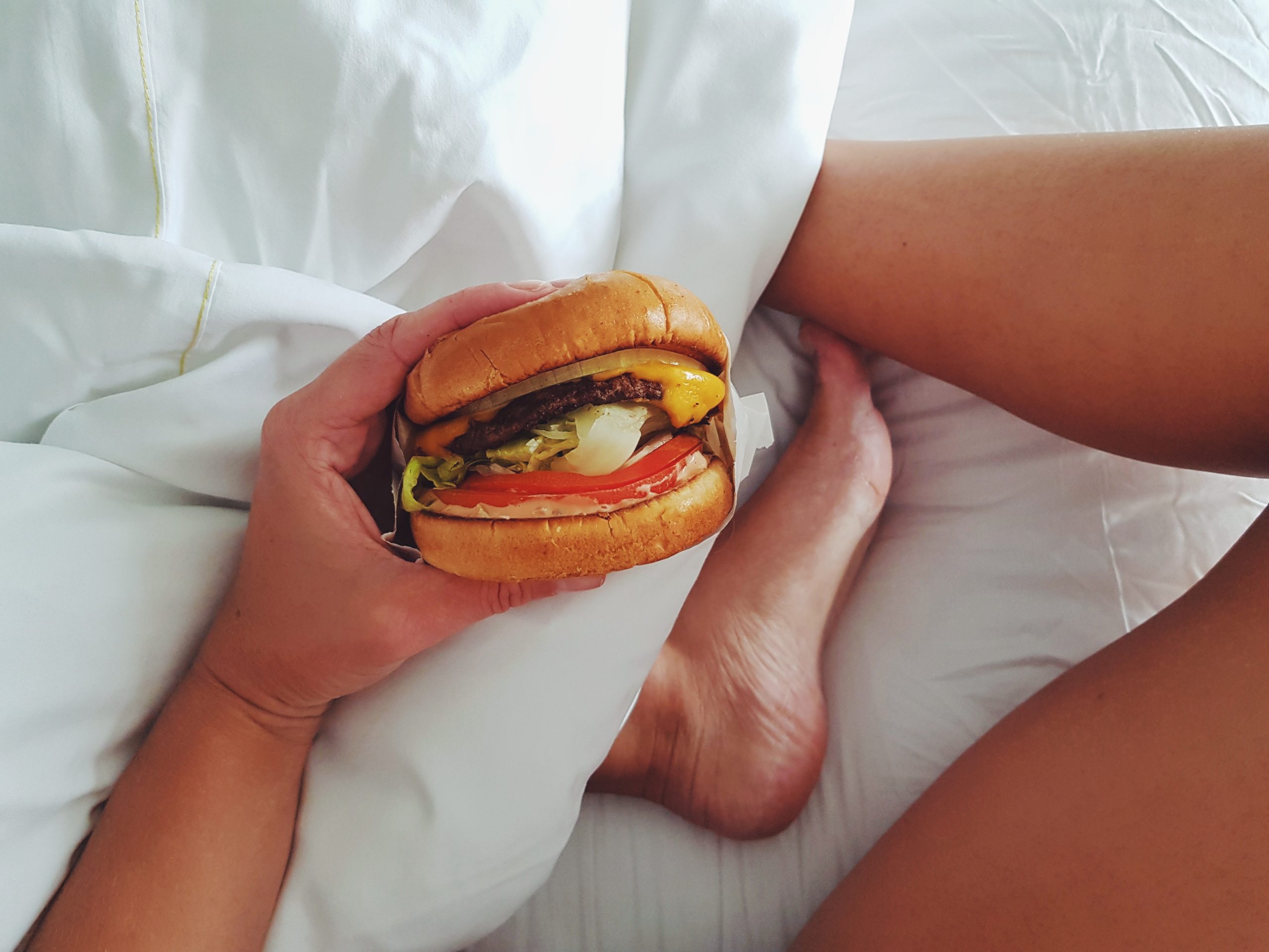 Frau isst Burger im Bett