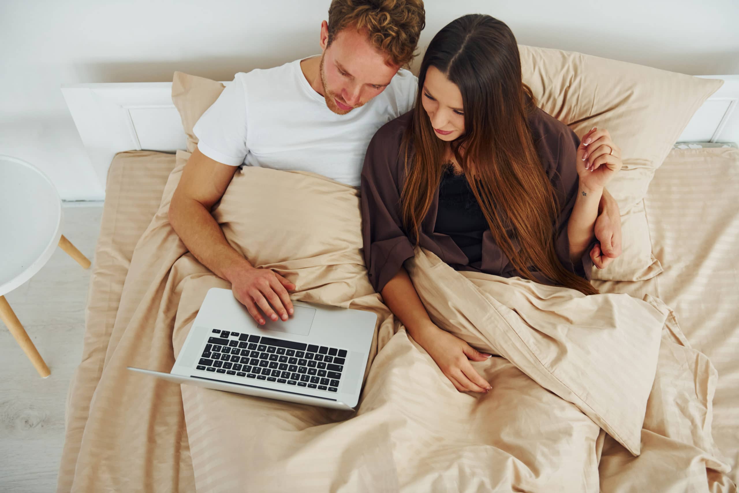 Paar liegt mit Laptop auf dem Bett