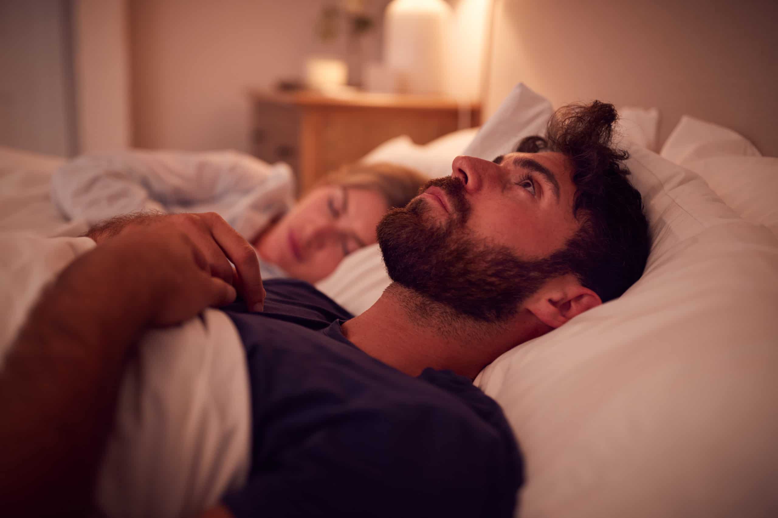 Paar mit Mann, der in der Nacht im Bett liegt und nachts unter Schlaflosigkeit leidet