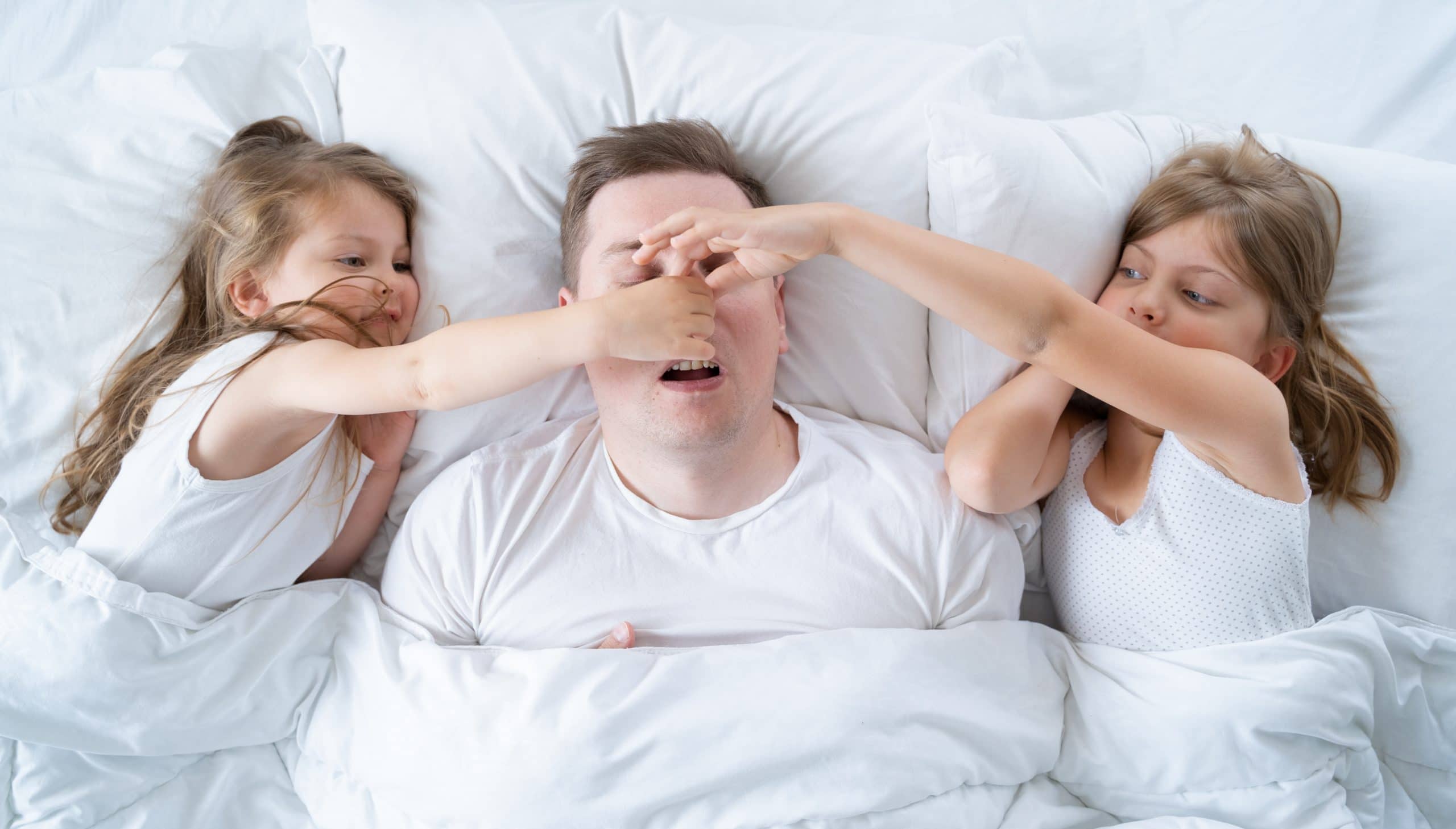 Vater schnarcht im Bett und Kinder halten Vater die Nase zu