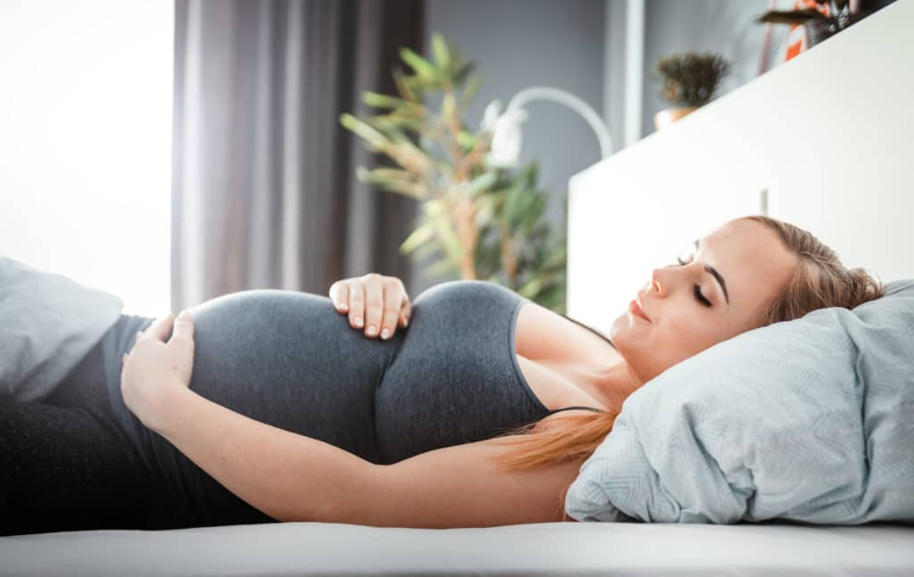 Junge schwangere Frau auf dem Bett berührt ihren Bauch