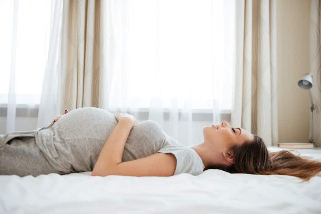 Lächelnd schwangere junge Frau liegend auf dem Bett