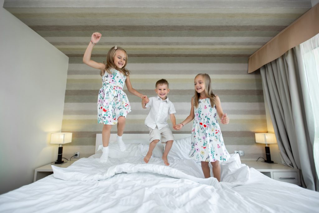 Glückliche Kinder, die auf dem Bett im Schlafzimmer springen, Spaß haben und spielen