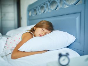 Kleines Mädchen schläft nachmittags zu Hause auf einer großen und gemütlichen weißen Bettwäsche