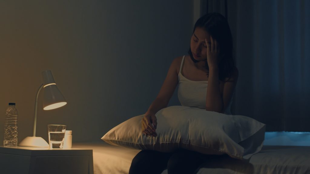 junge Frau, die auf dem Bett sitzt, nimmt Schlaftablette