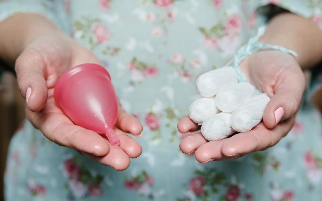 Frau hält Tampons und Menstruationstasse in Händen