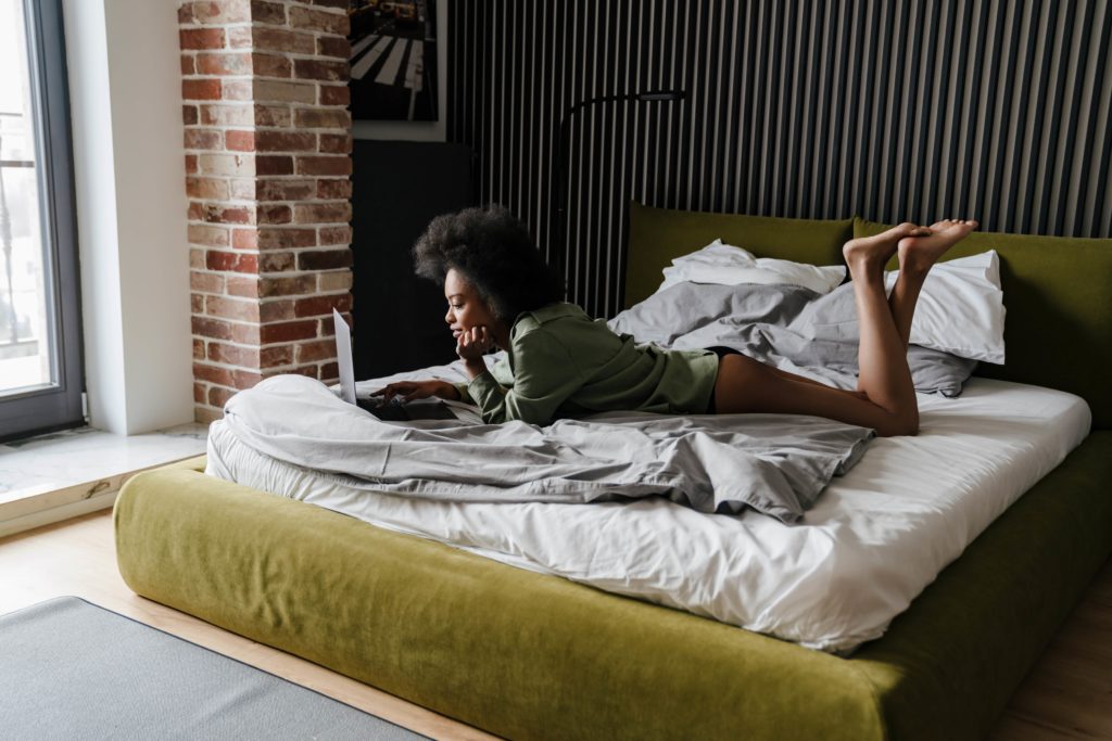 Frau benutzt Laptop nach dem Schlaf im Bett um sich über Periodische Bewegungsstörung der Gliedmaßen zu informieren