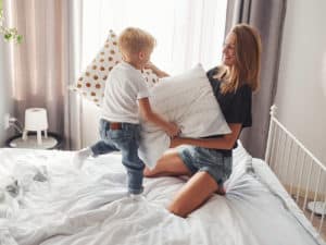 Mutter spielt tagsüber Kissenschlacht mit ihrem Sohn im Schlafzimmer