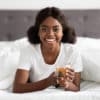 Fröhliche Afroamerikanerin genießt Kräutertee im Bett